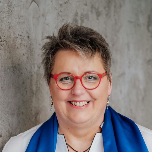 Christel Schilderink, kurze graue Haare und rote Brille, lächelt in die Kamera